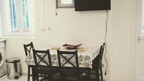 A dining area with a table, chairs, a TV mounted on the wall, and a window. - Historic district of Agde (Agde)