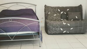 A bed with a metal frame and a purple mattress, a grey sofa with leaf patterns, and a small framed picture on the wall. - Historic district of Agde (Agde)