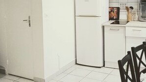 A kitchen with white cabinets, a refrigerator, a microwave, and a dining area with a chair and table. - Historic district of Agde (Agde)