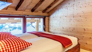 Un dormitorio de cabaña de madera con una cama, almohadones a cuadros y una colcha roja.