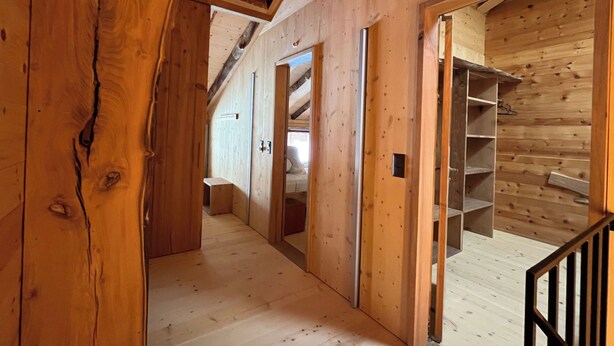 Un interior de madera con una escalera, estanterías abiertas y una puerta visible que conduce a otra habitación.