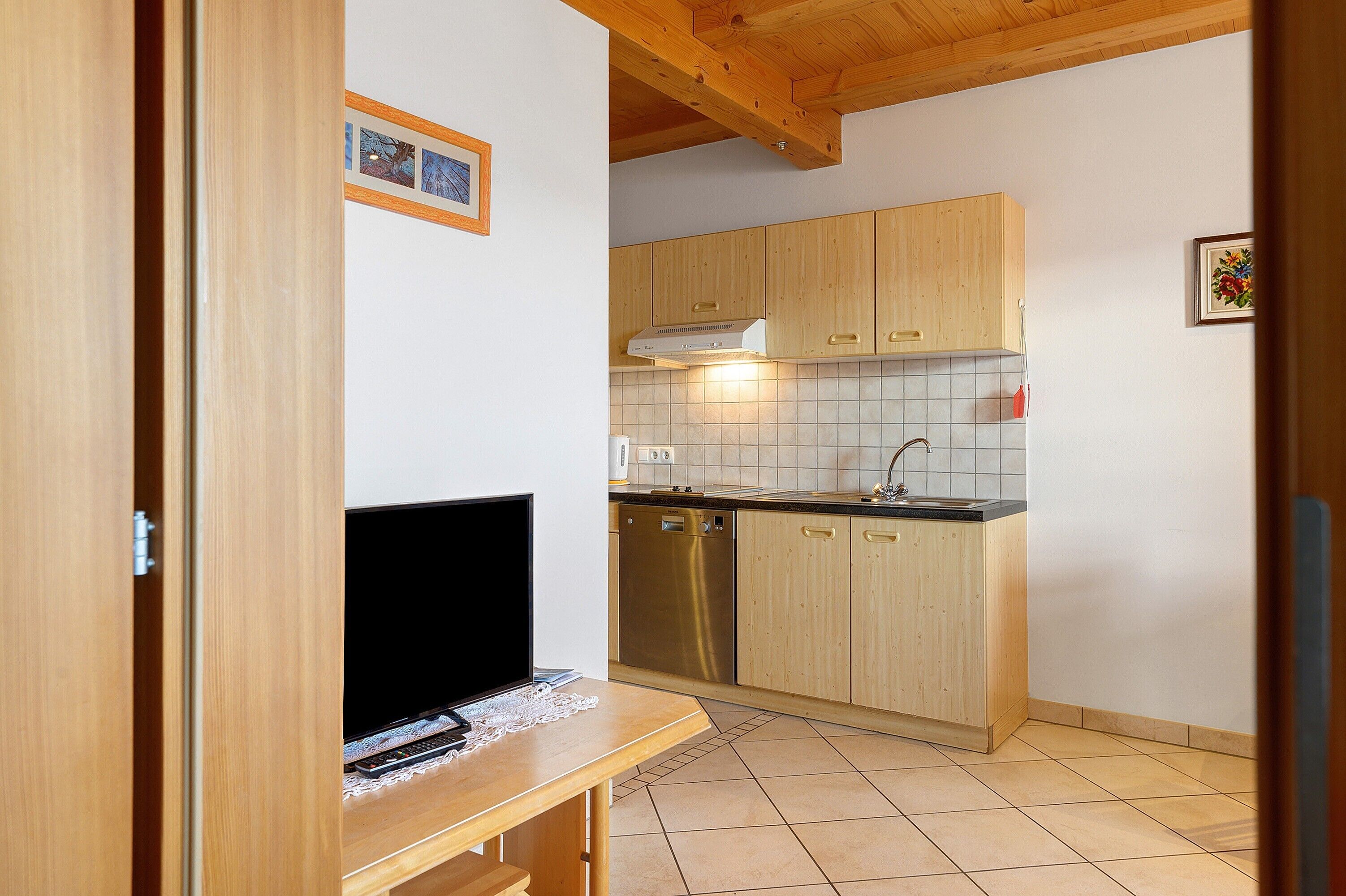 A kitchen with wooden cabinets, a dishwasher, and a television on a wooden table.