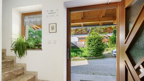 Eine Treppe führt zu einer Holztür, die in einen Garten mit einem geparkten Auto mündet.