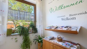 Ein Zimmer mit Fenster, einer Willkommensschild, einem Holzkasten und einem Regal mit Zeitschriften.