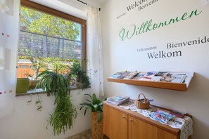 Ein Zimmer mit Fenster, einer Willkommensschild, einem Holzkasten und einem Regal mit Zeitschriften.