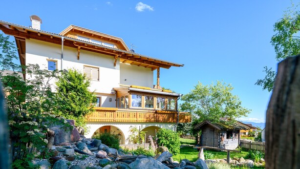 Ein zweistöckiges Haus mit einem Balkon, umgeben von einem Garten mit Steinen und Pflanzen.