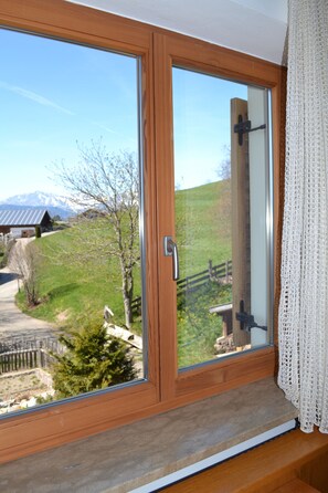 Ein Holzrahmenfenster mit Blick auf eine ländliche Landschaft, darunter ein Haus und ein Berg.