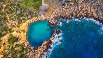 Vista aèria d'una zona costera amb terreny rocos, mar blava cristal·lina i una cala petita.