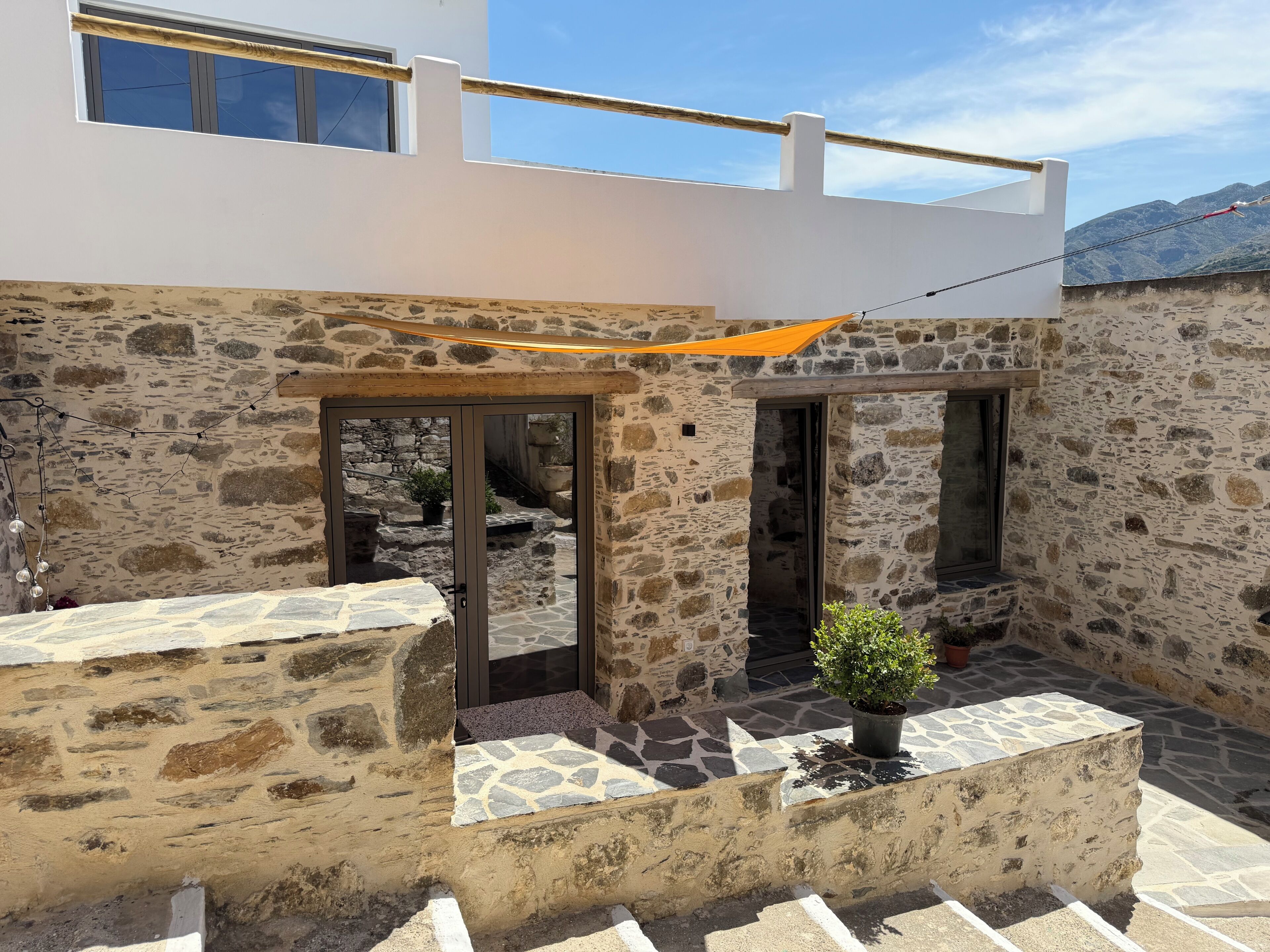 A stone building with a balcony, a potted plant, and a view of mountains.