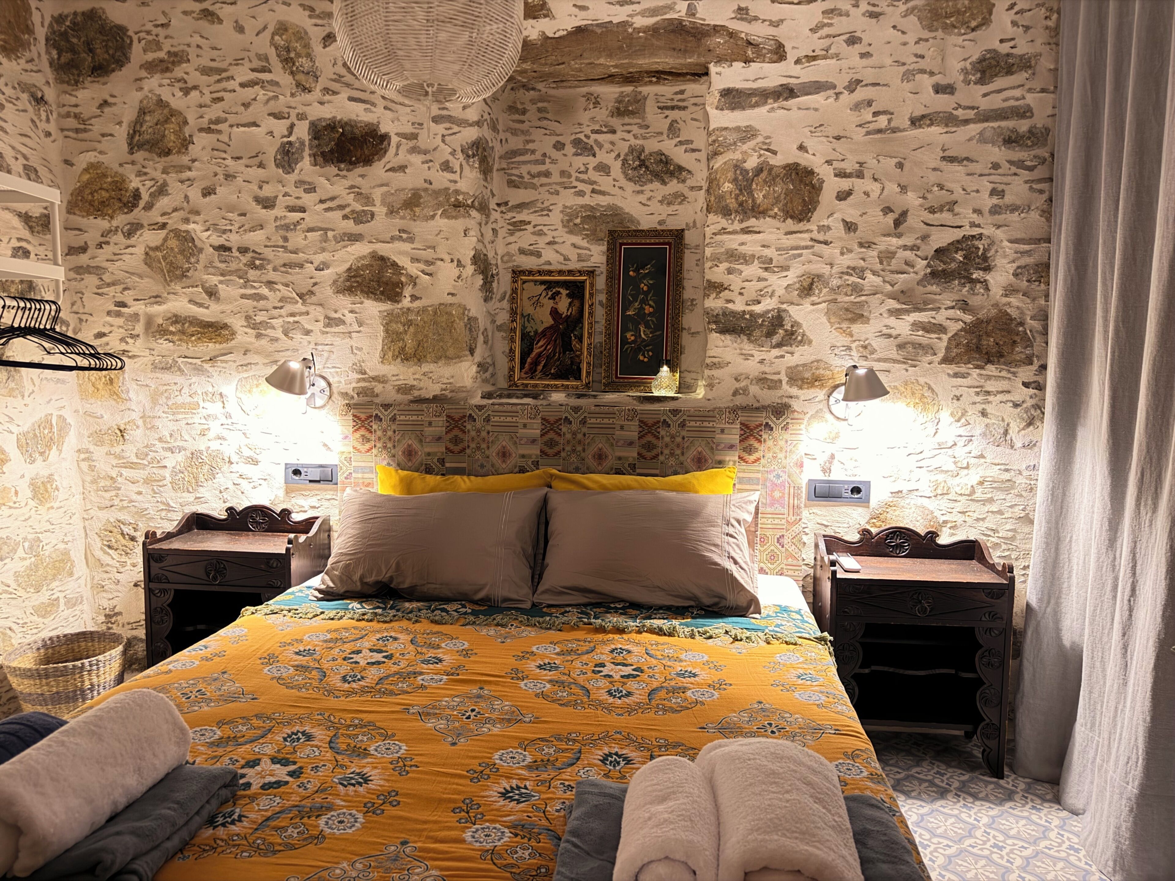 Een slaapkamer met een stenen muur, een bed met beddengoed met een patroon, twee nachtkastjes en een hangende lamp.