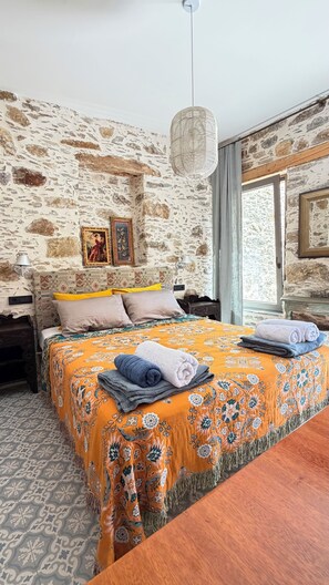 Ein Schlafzimmer mit einer Steinwand, einem Bett mit orangefarbenen Kissen und einem Vorhang, einer Hängeleuchte und einem Fenster mit Vorhängen.