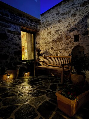 A stone courtyard with a wooden bench, potted plants, and a window with a view. - ELAFONISI PETRA HOUSE - Traditional Stone House near Elafonisi Beach 2BD, 2BTH (Kissamos, Chania)