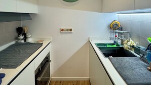 Een keuken met witte kastjes, een houten vloer, een wandklok en een spoelbak met een afwassysteem.