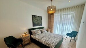 Een slaapkamer met een bed, nachtkastje, stoel, hanglamp en raam met gordijnen.
