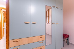 A wardrobe with multiple doors and drawers, a mirror, and a red chair in a room with light-colored walls. - Posada apartment a few minutes from the sea (Posada)