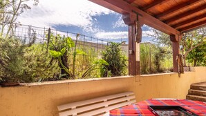 Un espace extérieur abrité, équipé d’une table, d’un banc et offrant une vue sur la verdure et une clôture.