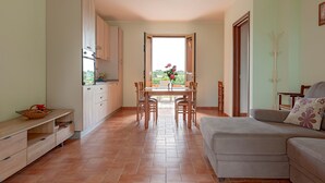 A modern kitchen with wooden cabinets, a dining table with chairs, a sofa, and a view through an open door. - Poggio Novello - Agriturismo Peccioli (Peccioli)
