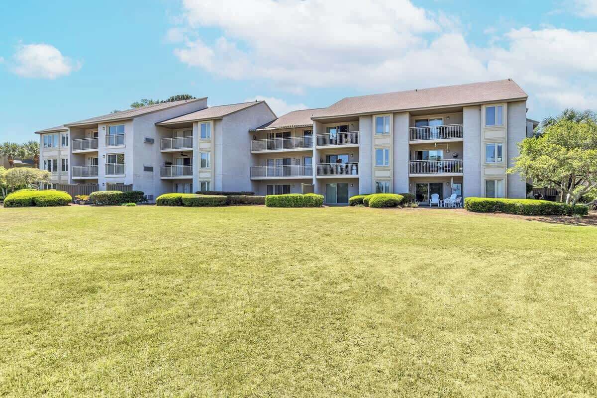 Multi-story vacation rental complex with private balconies overlooking expansive green lawn areas under bright blue skies.