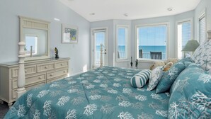 Een slaapkamer met een bed, een kaptafel en ramen met uitzicht op zee.