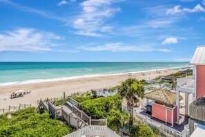 Blick auf einen Strand mit einer Holzpromenade, einem Gebäude mit einem Reetdach und Strandliegen.
