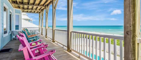 A wooden deck with colorful Adirondack chairs and a view of the ocean.