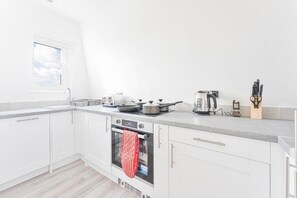Una cocina moderna con armarios blancos, horno empotrado, ventana y encimera con utensilios de cocina.