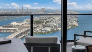 Ett hotellrum på hög höjd med ett stort fönster som vetter ut mot en stadsbild, inklusive en bro och en hamnfront.