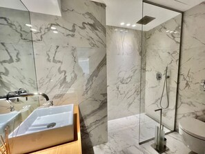 Ein modernes Badezimmer mit Marmorwaschtisch, Duschkabine aus Glas und Holzwaschbecken.