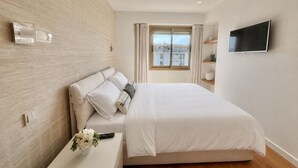 Une chambre moderne avec un lit, une télévision, une fenêtre avec des rideaux et une vue sur les bâtiments environnants.