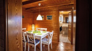 A wooden interior with a dining table, chairs, a hanging light fixture, and a visible bathroom.