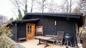 A wooden cabin with a tiled patio, a wooden bench, a table, and a grill.