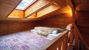 A small, wooden attic bedroom with a skylight, a bed with a blanket, and a patterned rug.