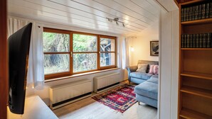A room with a large window, a sofa, a television, and a bookshelf.