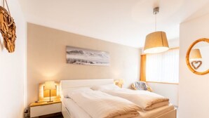 A bedroom with a bed, bedside lamps, a wall-mounted picture, a window with curtains, and a hanging lamp. - Crap Uaul by Interhome (Flims)