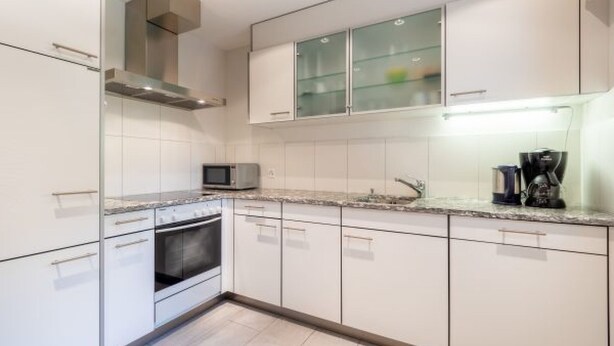 A modern kitchen with white cabinets, a microwave, a coffee maker, and a built-in oven. - Crap Uaul by Interhome (Flims)