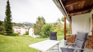 A patio with a table and chairs, a wooden ceiling, and a view of a building and trees. - Crap Uaul by Interhome (Flims)