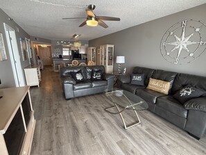 Ein Wohnzimmer mit grauem Sofa, einem Glastisch, einem Deckenventilator und einer Kompass-Wanddekoration.