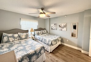 Une chambre avec deux lits, un ventilateur de plafond, une fenêtre avec des stores et des œuvres d’art murales.