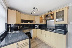 Une cuisine moderne avec des meubles en bois, un plan de travail noir, des appareils en acier inoxydable et un four encastré.