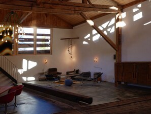 A spacious room with a wooden ceiling, a staircase, and a large window allowing natural light. There are two chairs and a table, and a small exercise ball. - Ferienhaus Stalla d'Immez, (Sta. Maria - Santa Maria Val Müstair) by Interhome (Sta. Maria GR)
