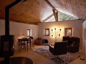 A cozy room with a wooden ceiling, a fireplace, a dining table with chairs, a sofa, and a rug. - Ferienhaus Stalla d'Immez, (Sta. Maria - Santa Maria Val Müstair) by Interhome (Sta. Maria GR)