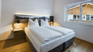 Een slaapkamer met een bed, houten hoofdbord, bedlampen, een raam met uitzicht en een houten vloer.