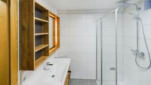 Een badkamer met een houten wastafelmeubel, een douchecabine en witte betegelde wanden.