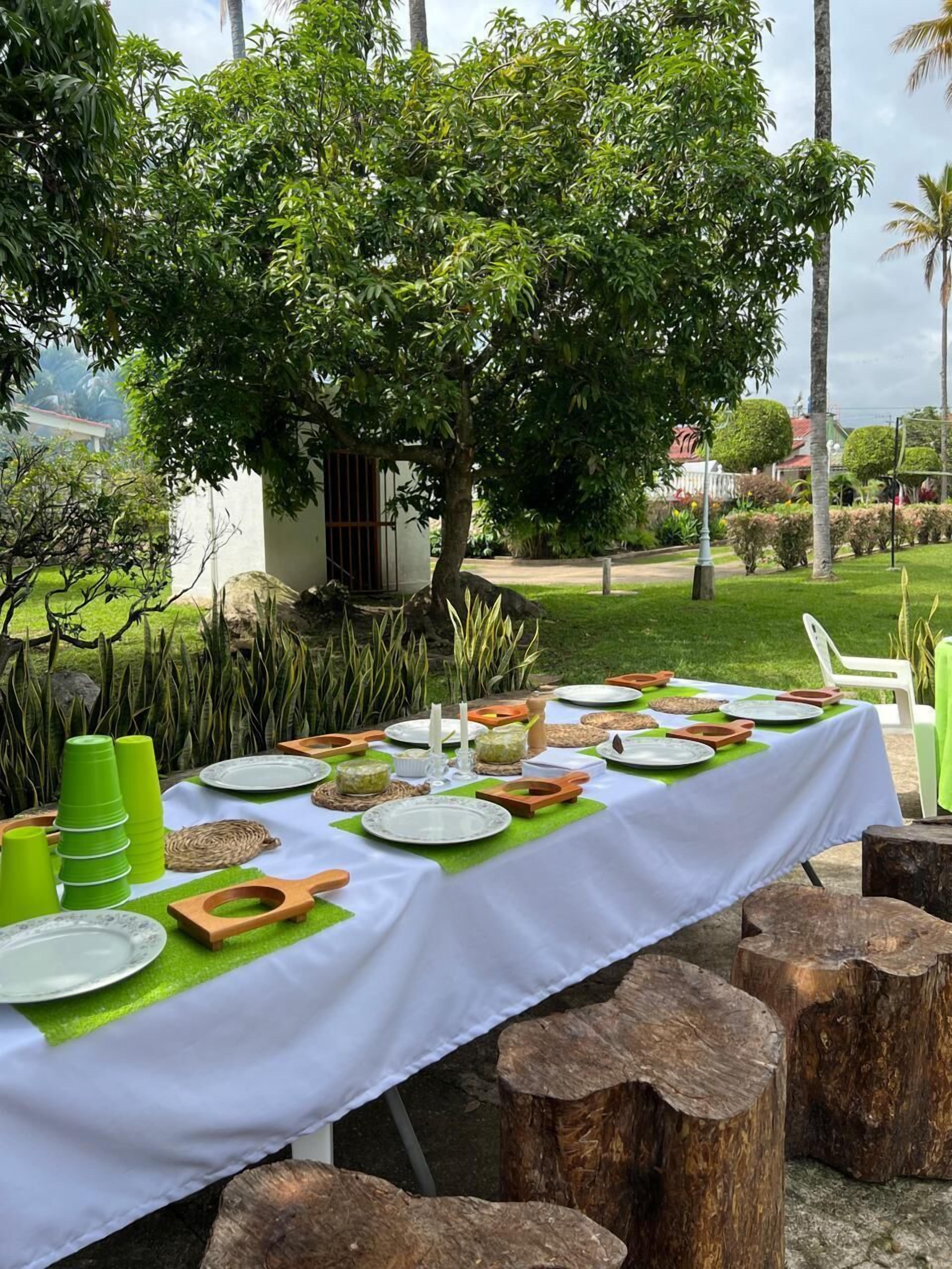 Un espacio para comer al aire libre con una mesa lista para una comida, rodeado de follaje y árboles.