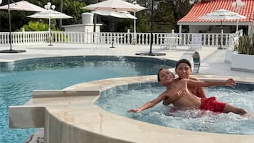En swimmingpool med et boblebad, omgivet af palmer og parasoller.