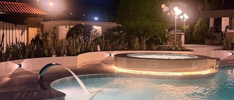 Una piscina con hidromasaje y fuente de agua por la noche.