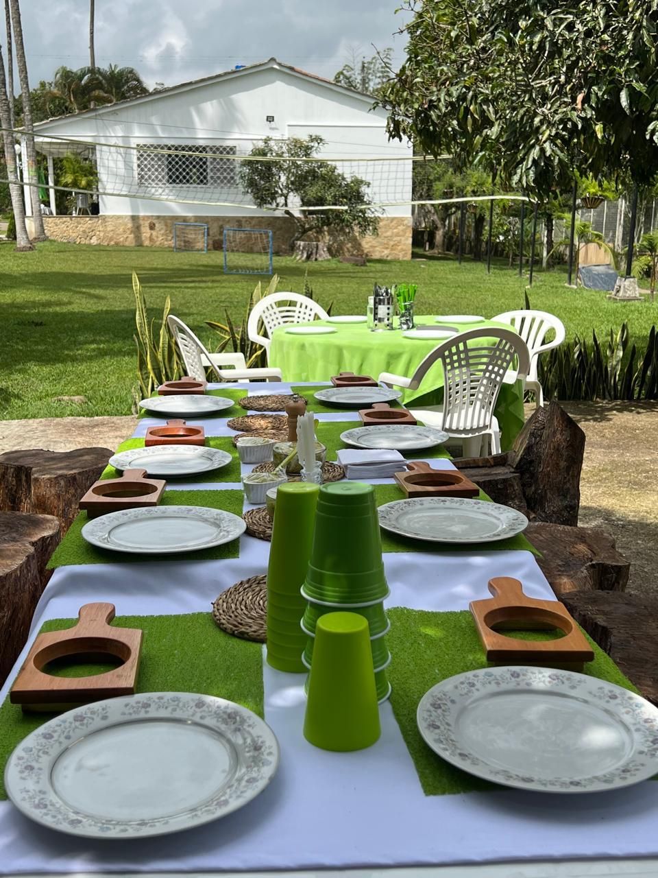 Un área de comedor al aire libre con una mesa preparada para cuatro personas, rodeada de sillas y una casa al fondo.