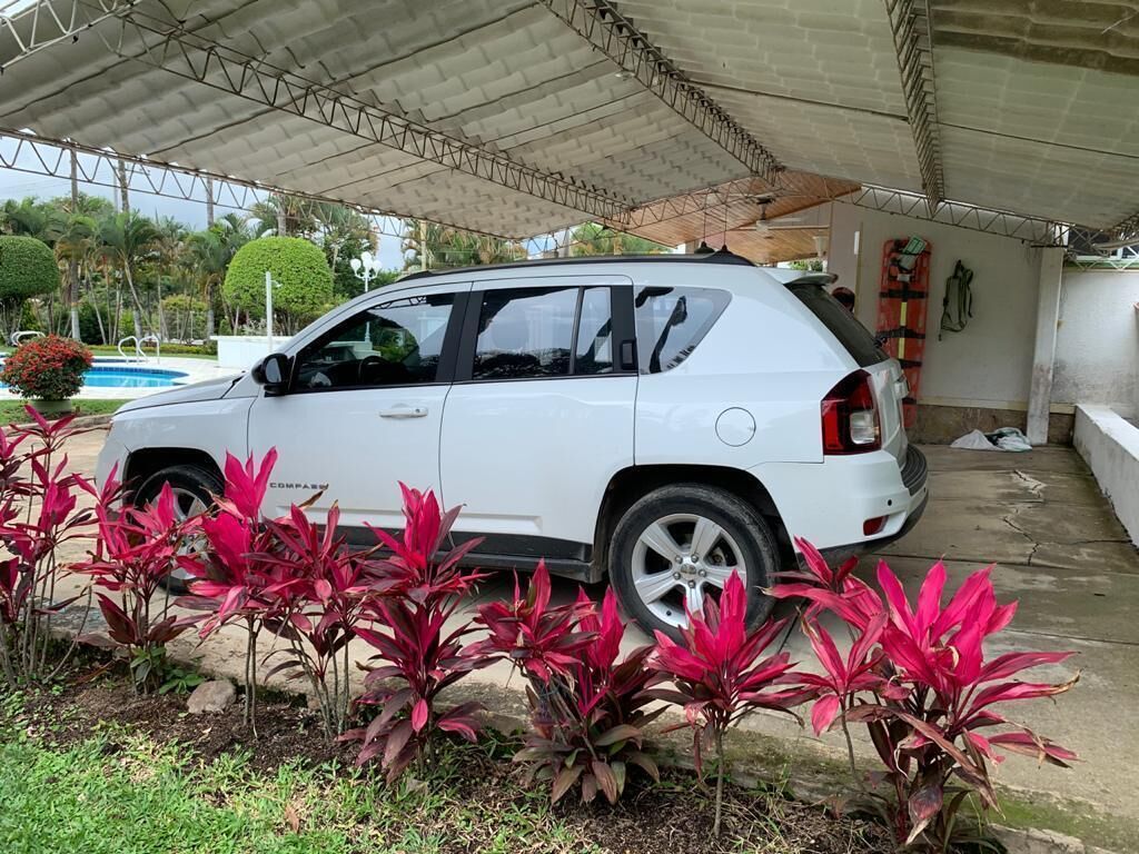En vit SUV står parkerad under ett tak, och i bakgrunden syns en pool.
