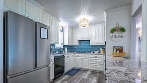 A kitchen with white cabinets, a stainless steel refrigerator, a dishwasher, and a blue tiled backsplash. - Never a Bad Day at PK Lake- Waterfront, Pool Table, Firepit (Graford)
