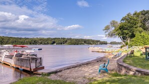 Une jetée au bord du lac avec des bateaux, une plage de sable et une zone herbeuse avec un banc.